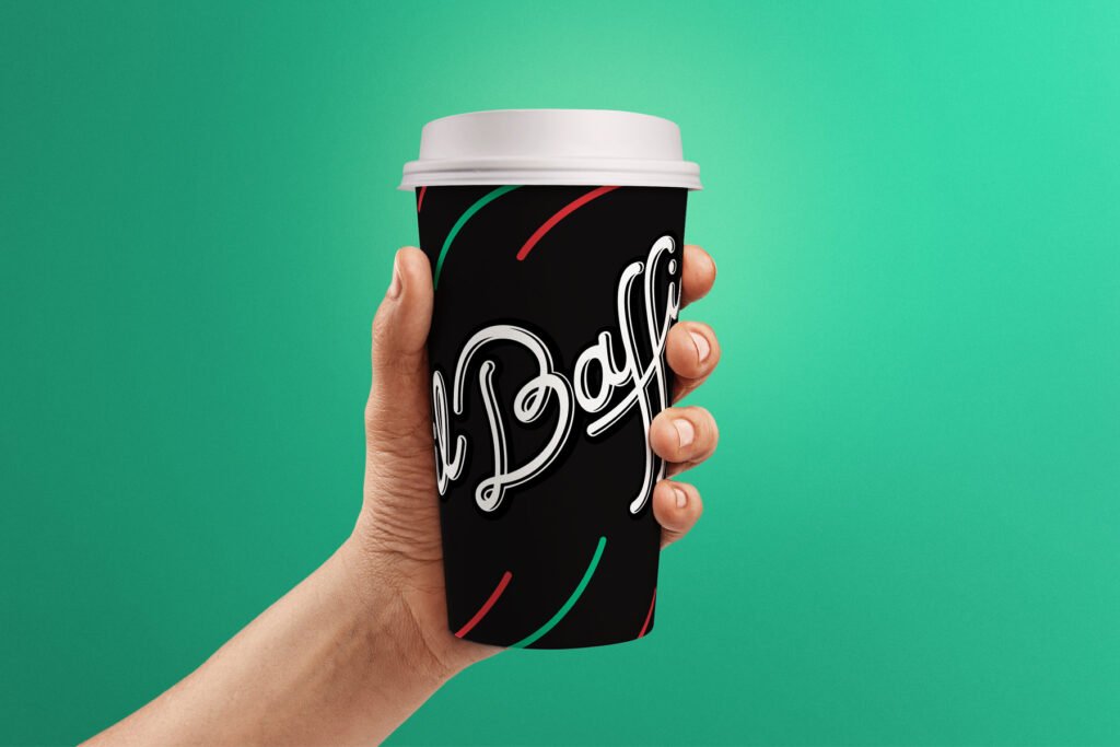 A designer hand holds a black takeaway coffee cup with colorful curved lines and cursive white text, set against a bright green background. The cup features a creative direction with a sleek white lid. - FelipeIgiesias.com