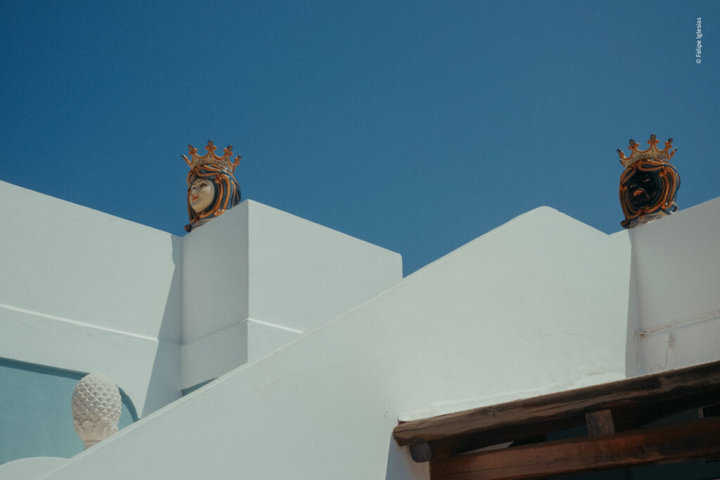 Over a white traditional Aeolian house, two ceramic "Teste di moro" contrasting the blue sky - photography by Felipe Iglesias