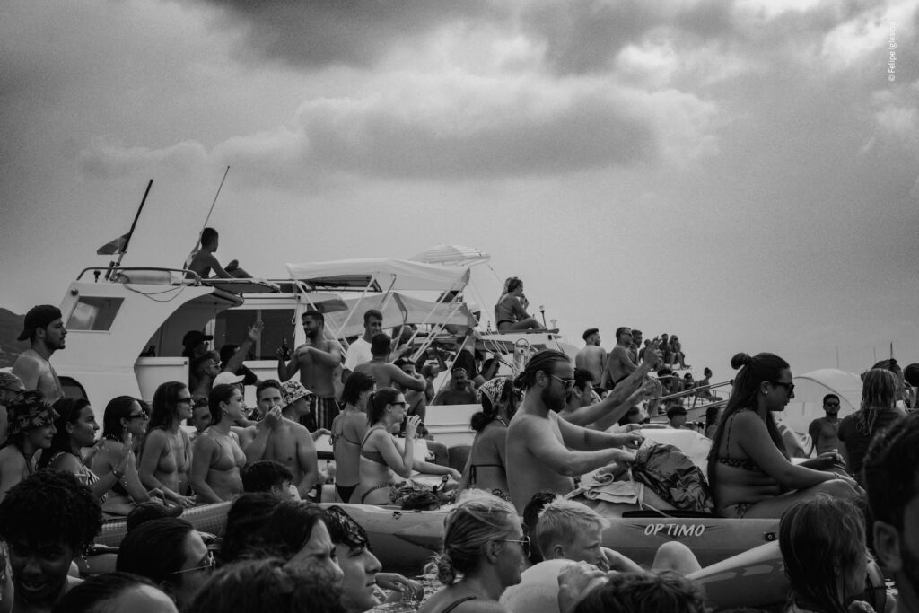 Chaotic and lively crowd awaiting the results of the 'Ntinna a Mari' event in Cefalù, seated on various boats, tenders, and zodiacs beneath a moody, overcast sky – photography by Felipe Iglesias.