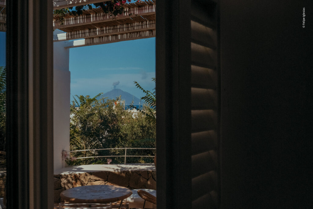 Shaded patio with furniture, pergola flowers, mountain with smoke under blue sky in the background - picture by Felipe Iglesias